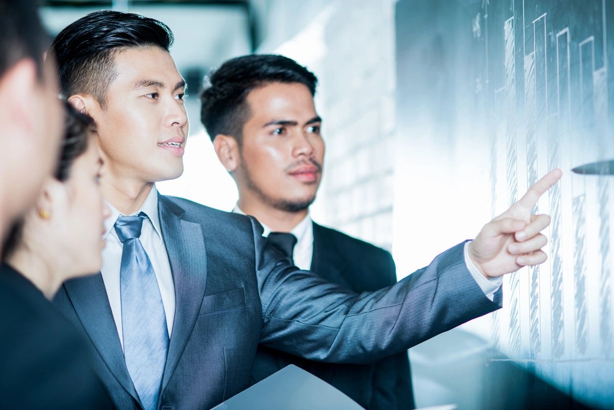 Two men in suits are looking at a glass board.